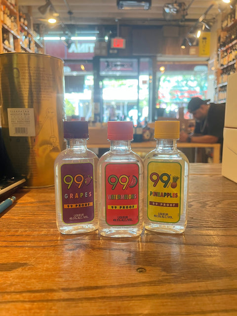 Three small plastic bottles with colorful labels that say 99 and their respective flavors, from left to right grape, watermelon, pineapples.