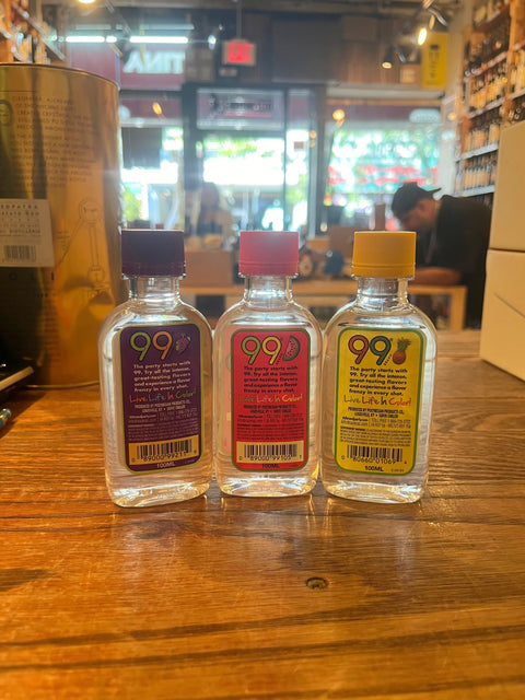 Three small plastic bottles with colorful labels that say 99 and their respective flavors, from left to right grape, watermelon, pineapples.