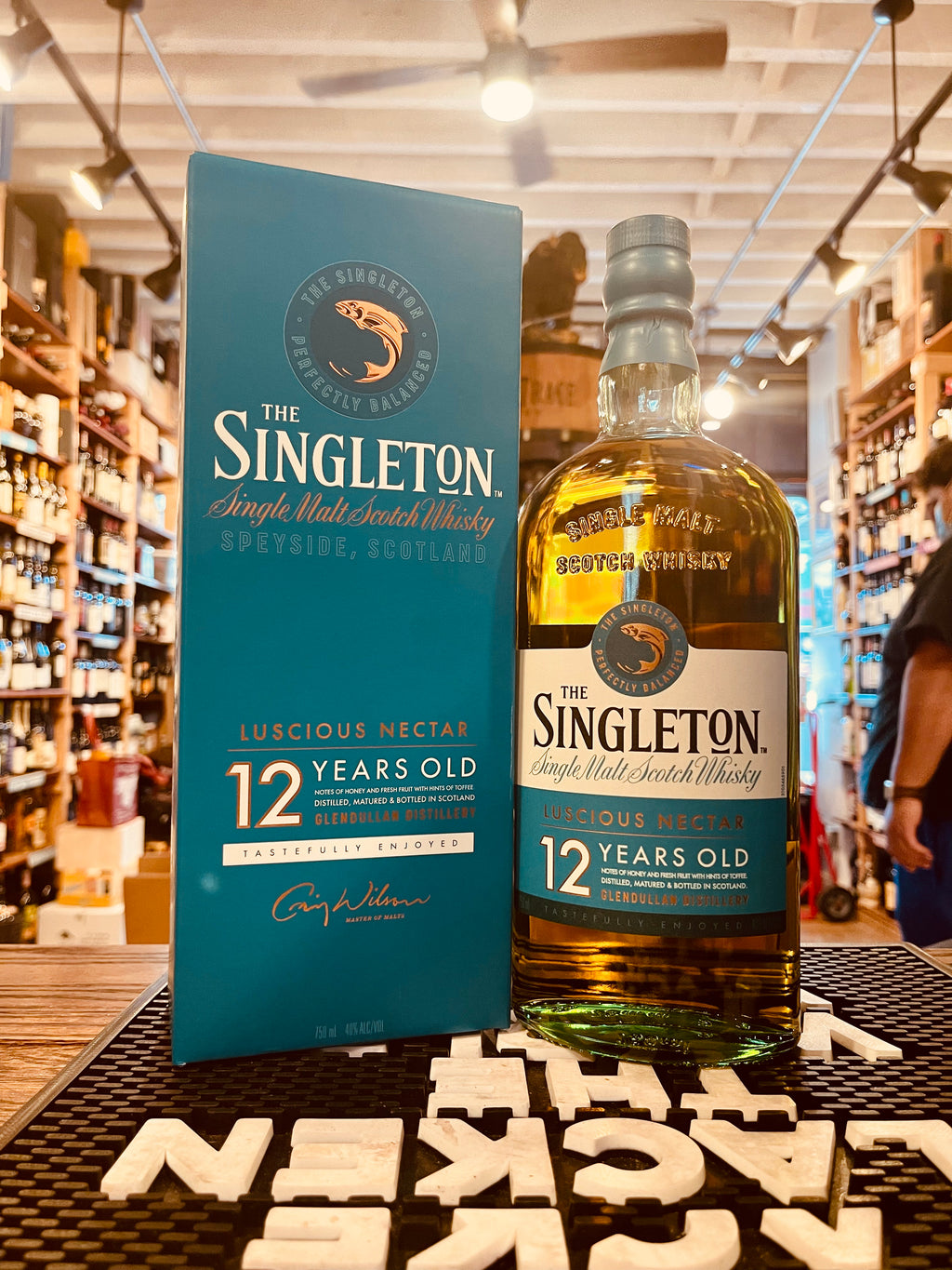 Singleton Luscious Nectar Single Malt 12Yr 750mL a aqua blue square box next to a flat surface clear bottle with rounded shoulders and a white and aqua green label and a aqua green top