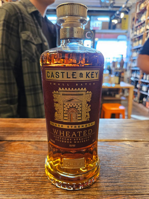 Castle and Key Cask Strength Wheated Bourbon 750mL a broad shouldered clear glass bottle with a red label and golden top