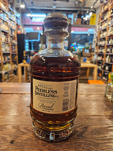 Peerless Bourbon Rum Barrel Finished 750mL a short squat rounded clear glass bottle with a beige and green label with a wooden top