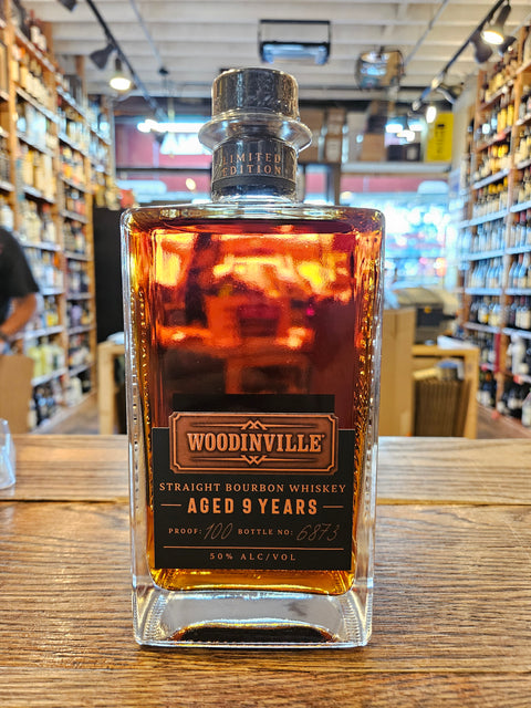 Bottle of Woodinville Straight Bourbon Whiskey Aged 9 Years on a wooden surface with store shelves in the background.