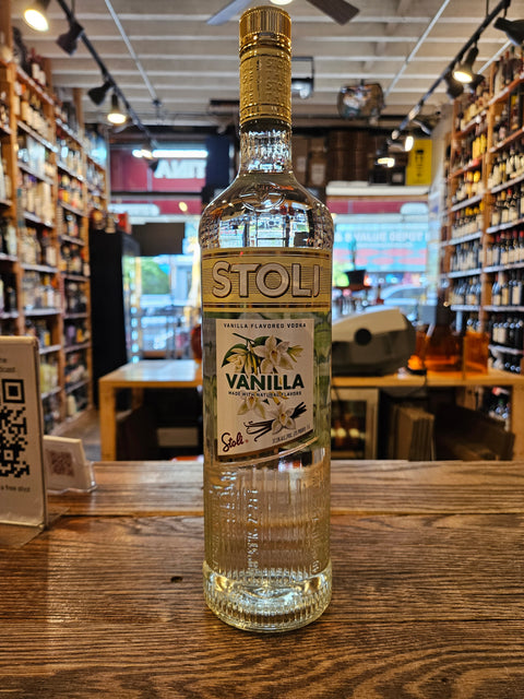 Bottle of Stoli Vanilla vodka on a wooden surface with a blurred indoor background