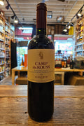 Wine bottle labeled 'Camp du Rouss' on a wooden surface with a store interior in the background