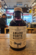 Bottle of Mazzetti Amando Forte liqueur on a wooden surface with a store interior in the background.