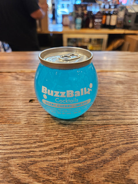 Blue BuzzBallz cocktail can on a wooden surface with a blurred bar background