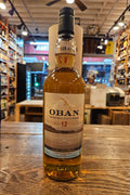 Oban 12-year-old whisky bottle on a wooden surface with a store interior in the background