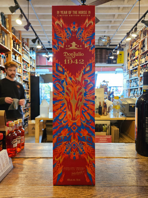 Bottle of Don Julio 1942 tequila on a wooden surface with a colorful label.