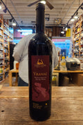 Bottle of Vranac wine on a wooden surface with a blurred store interior in the background.