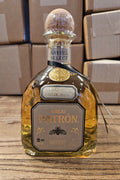 Patrón tequila bottle on a wooden surface with boxes in the background