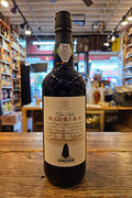 Bottle of Madeira wine on a wooden surface with a blurred store interior in the background
