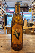 Bottle of Nixta tequila on a wooden surface with a store interior in the background