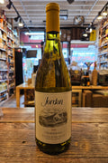 Bottle of Jordan Chardonnay wine on a wooden surface with a store interior in the background