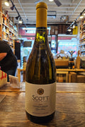 Bottle of Scott Chardonnay wine on a wooden surface with a store interior in the background.