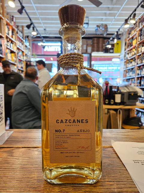 Bottle of Cazcanes tequila on a wooden surface with a blurred indoor background