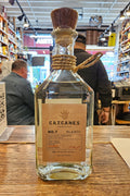 Bottle of Cazcanes Blanco tequila on a wooden surface with a store interior in the background.