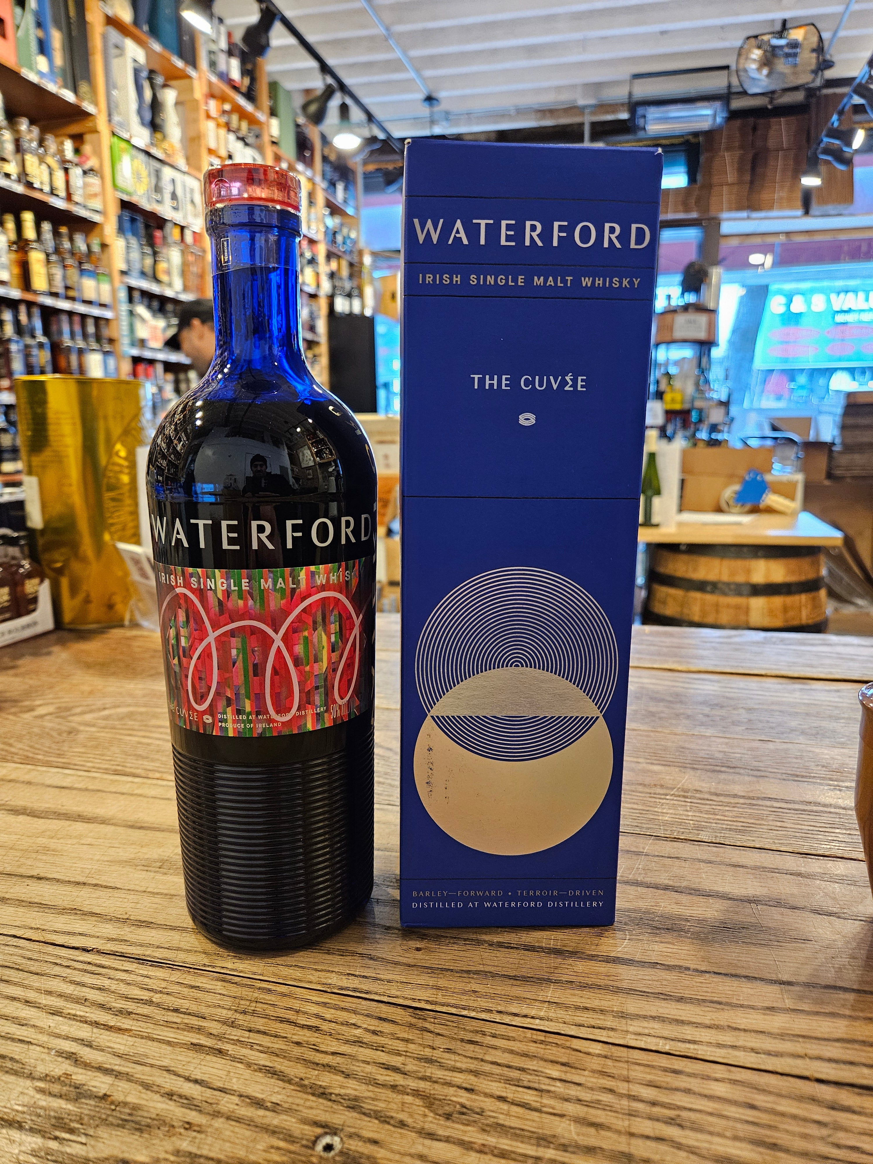 WaterFord THE CUVÉE 750mL a blue bottle with ripple glass bottom and a colorful red label with a red glass top, next to a tall blue box