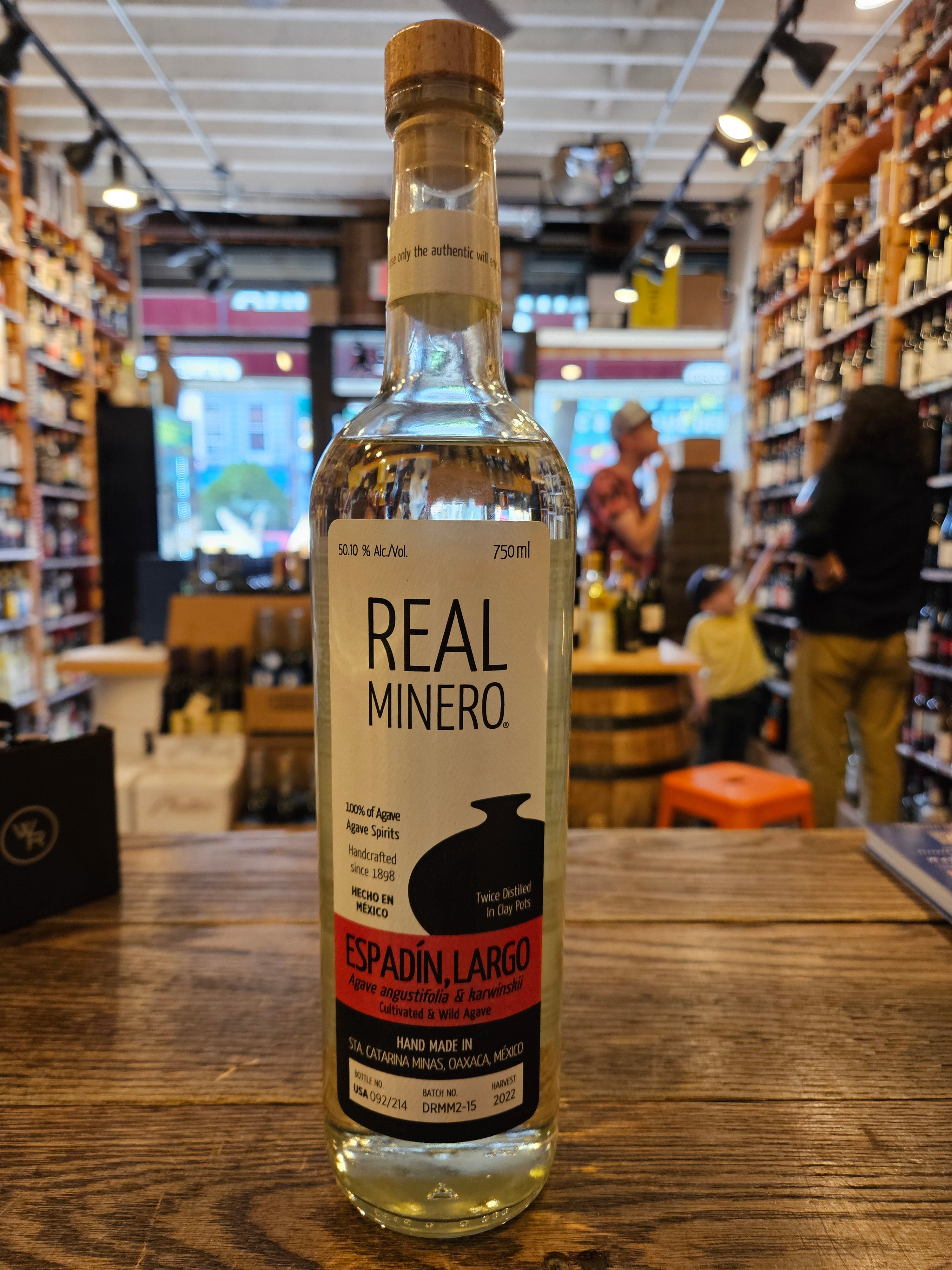 Real Minero Espadin Largo 750mL a tall clear glass bottle with a white, red, and black label with a wooden top