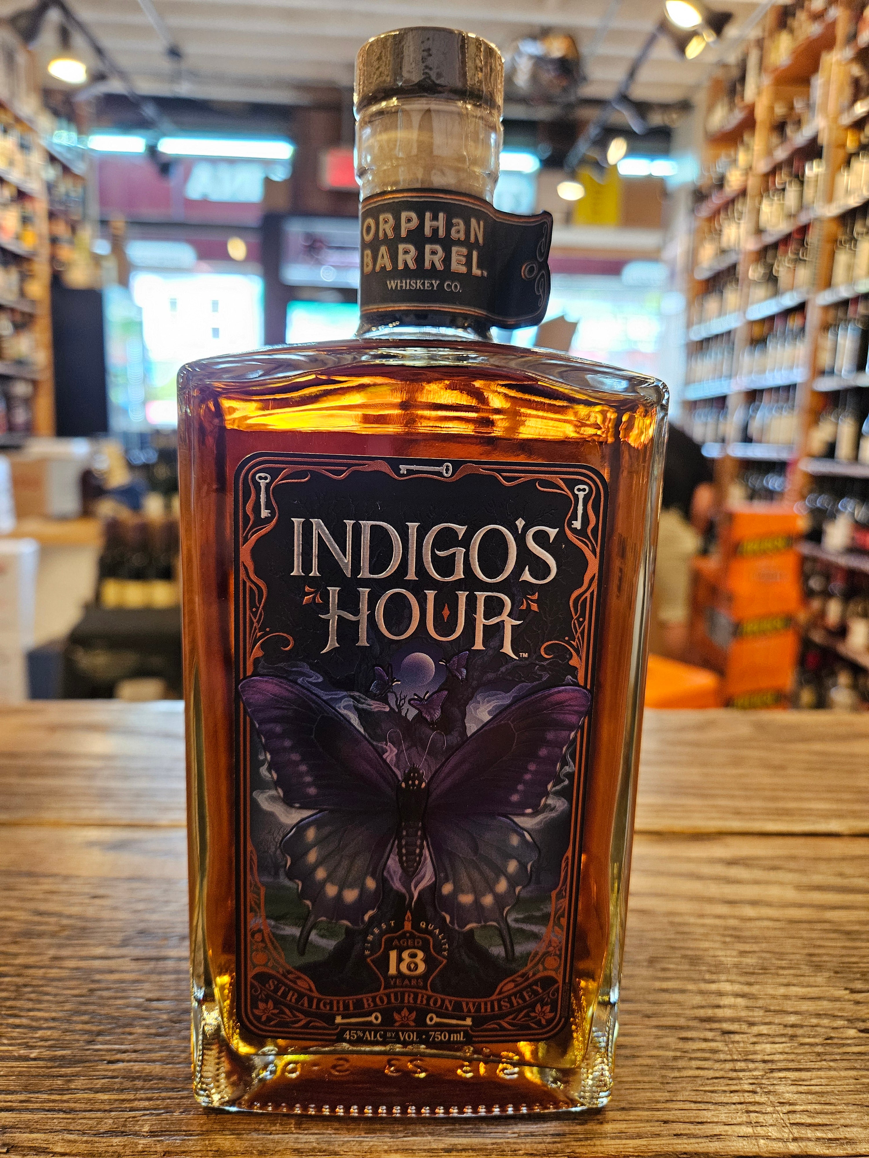Orphan Barrel Indigo's Hour 750mL a squared short clear glass bottle with a black and indigo label and a wooden top