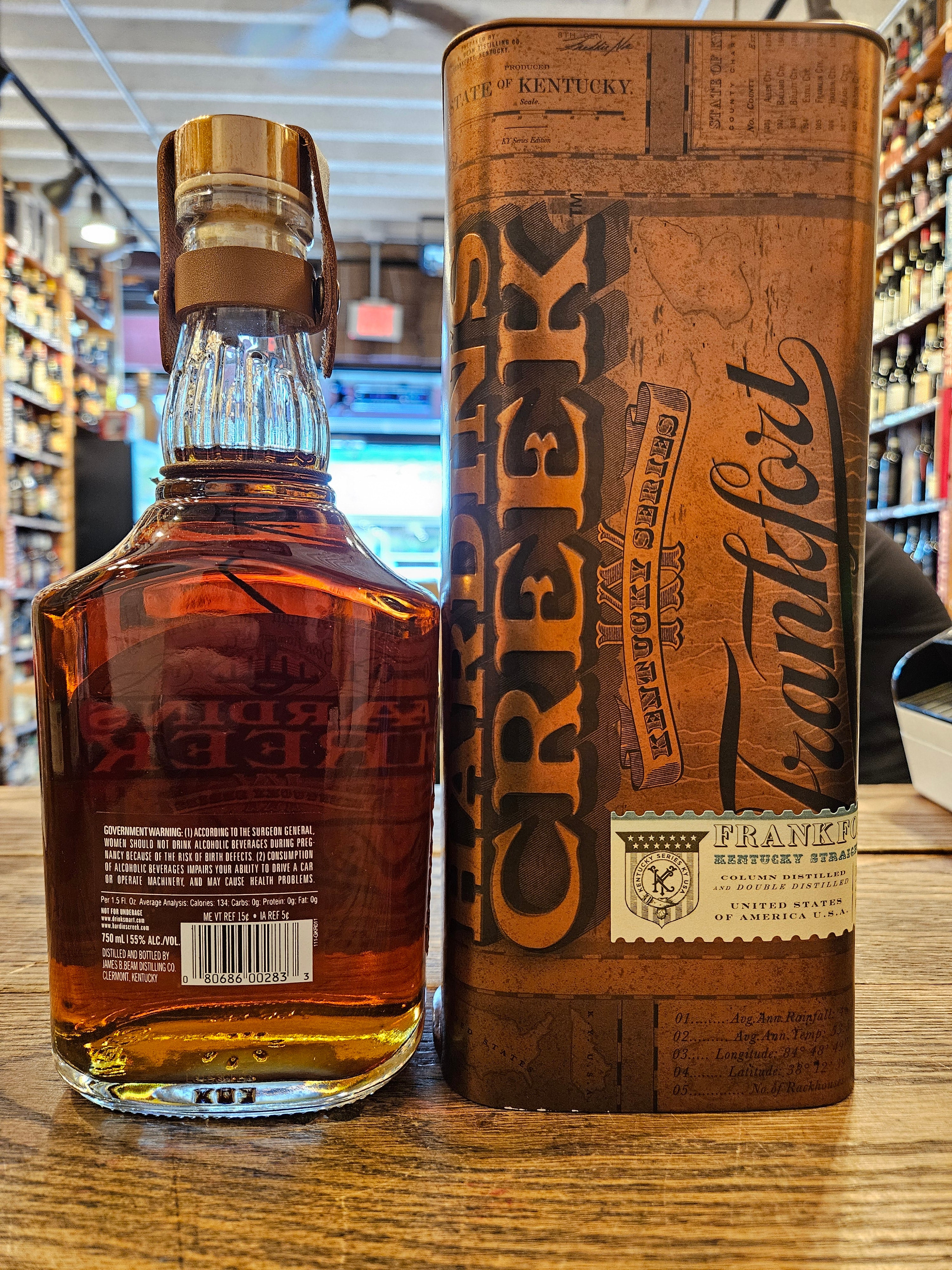 Hardin's Creek Kentucky Straight Bourbon Whiskey Frankfort 750mL the backside of a clear glass squared bottle with a fat neck, a white label, and a copper top, next to a rectangular shaped copper colored box. 