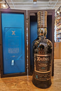 Ardbeg Vintage Y2K 23 Year Old Single Malt Scotch Whisky 700mL a dark glass bottle with a black and silver label and black top. Standing in front of a black open wooden box with a blue lining