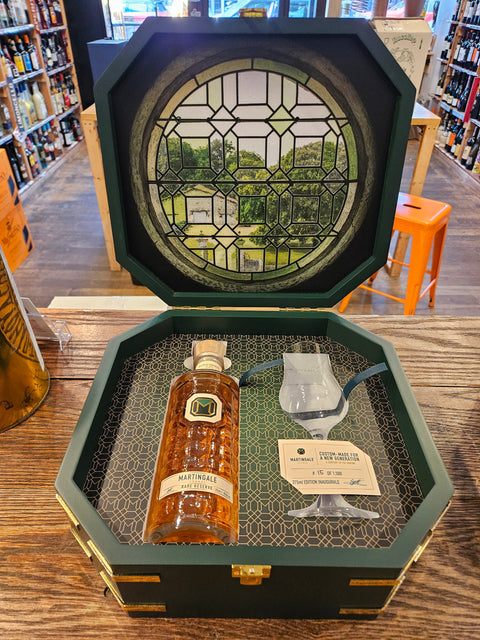 Martingale Cognac Gift Set 375mL a short clear glass bottle with indentations next to a thin stemmed glass inside an open green wooden box