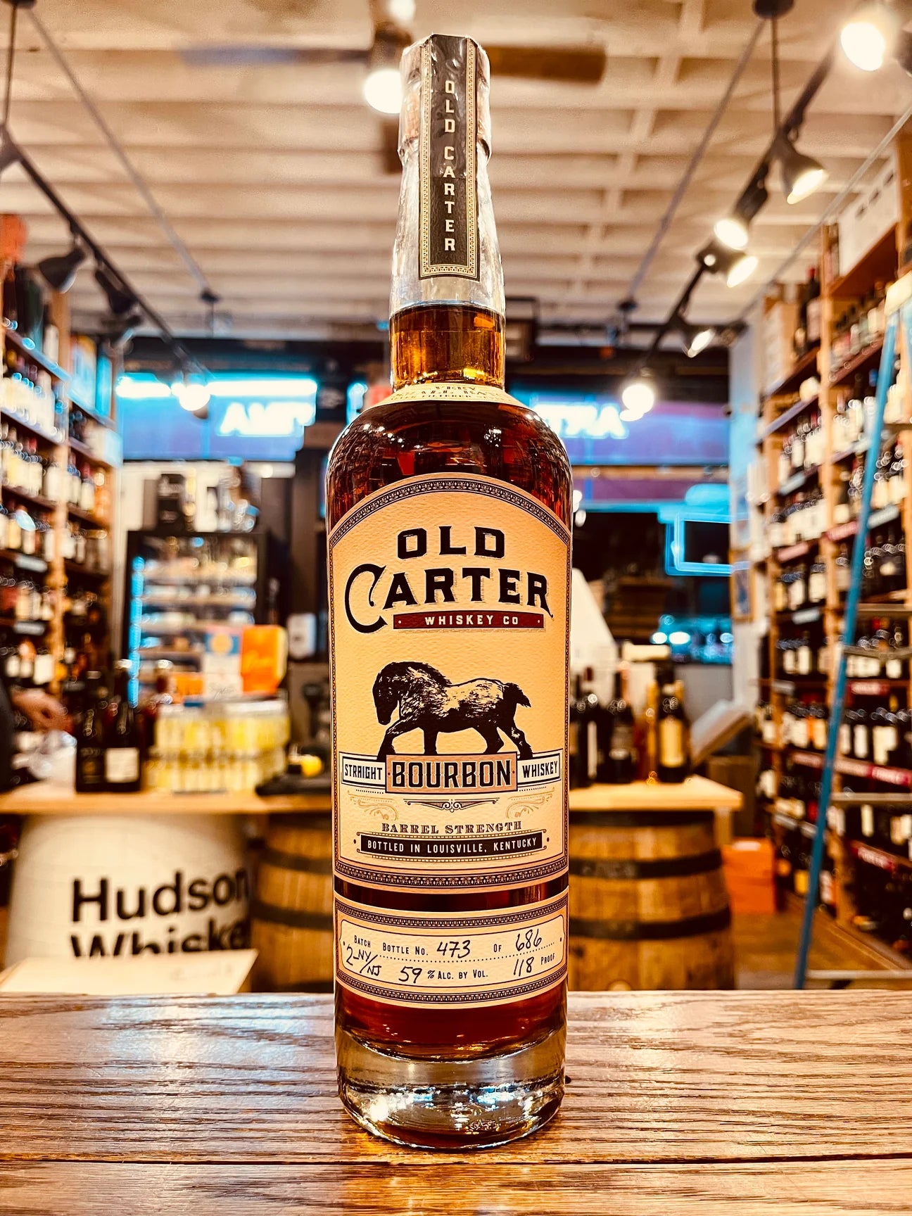 Old Carter Bourbon Whiskey Barrel Strength Very Small Batch 750mL Batch 3-NY/NJ a tall high shouldered slender necked clear glass bottle with a beige label and the image of a horse on it with a wooden topper
