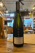 Green wine bottle with wide shoulders, the label is navy blue geometric shapes circles on top and white on bottom with labels saying versalto pinot bianco alois lageder