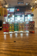 Small clear bottles with colorful labels that read 99, from left to right watermellon, bananas, apples, butterscotch, peppermint, and xpresso coffee, and 99 proof