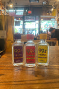 Three small plastic bottles with colorful labels that say 99 and their respective flavors, from left to right grape, watermelon, pineapples.
