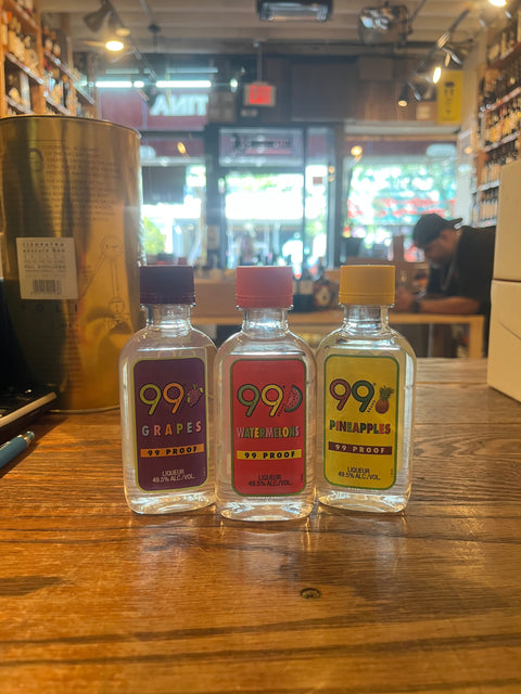 Three small plastic bottles with colorful labels that say 99 and their respective flavors, from left to right grape, watermelon, pineapples.