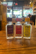 Three small plastic bottles with colorful labels that say 99 and their respective flavors, from left to right grape, watermelon, pineapples.