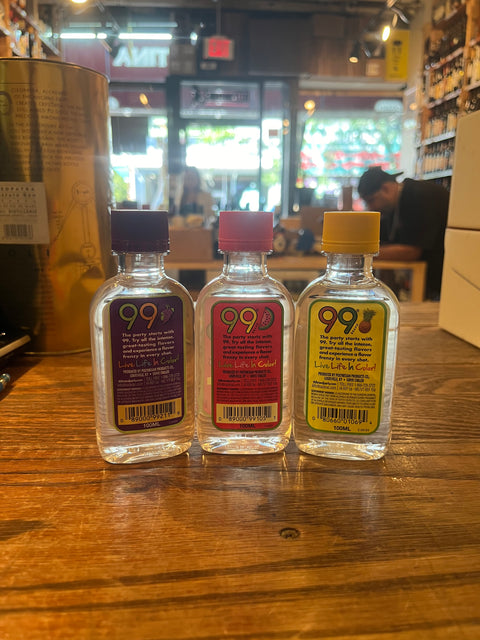 Three small plastic bottles with colorful labels that say 99 and their respective flavors, from left to right grape, watermelon, pineapples.