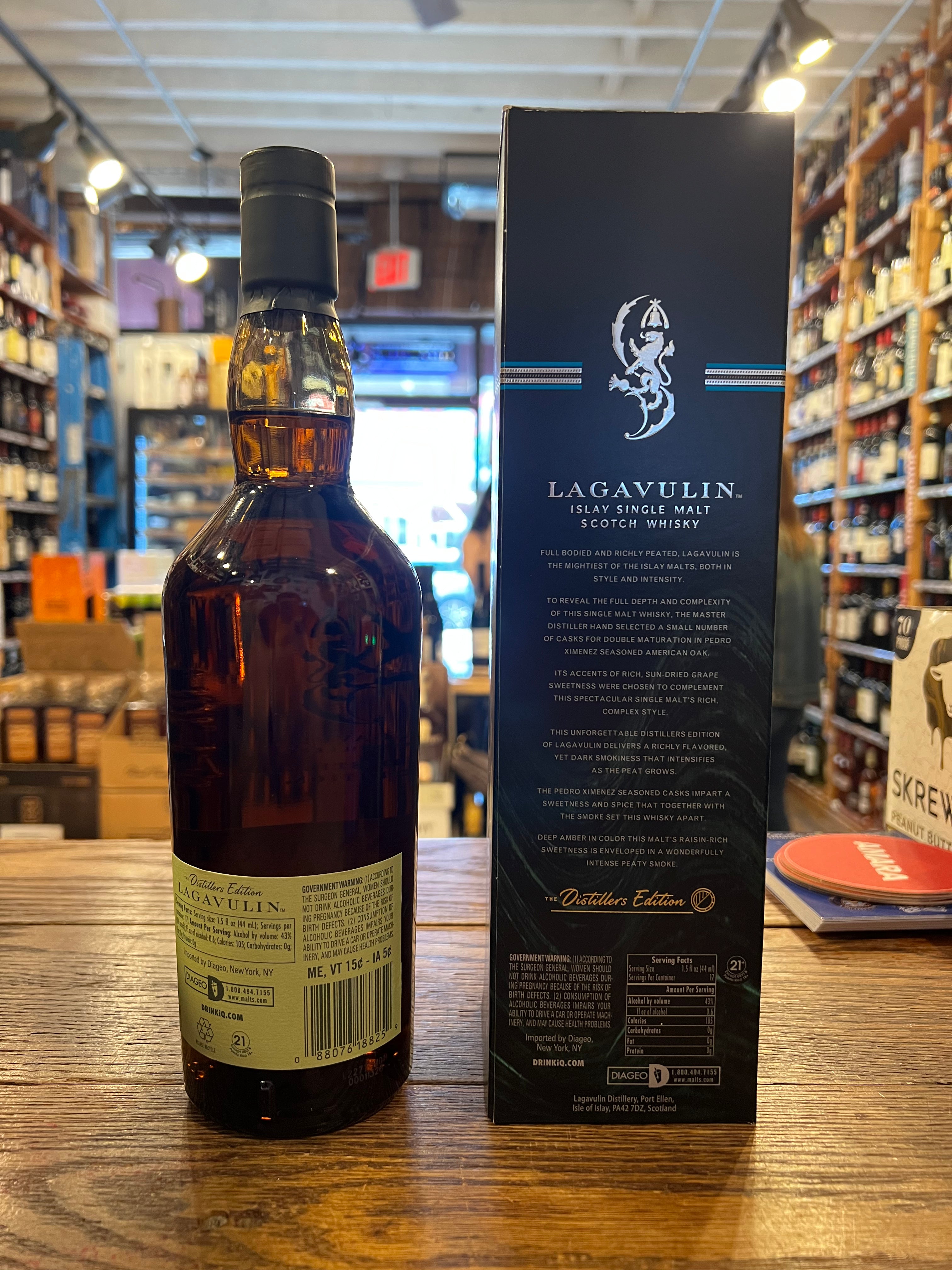 Lagavulin Distillers Edition Islay Single Malt 750ml the backside of a tall round shouldered clear glass bottle with a light green label and dark green top next to a tall squared dark blue box