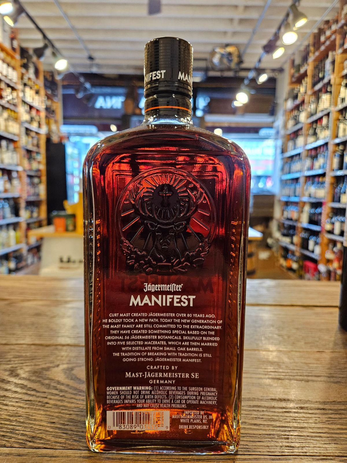 Jagermeister Manifest 1L the backside of a tall flat surfaced squared clear glass bottle with white lettering and a deer head etched into the glass
