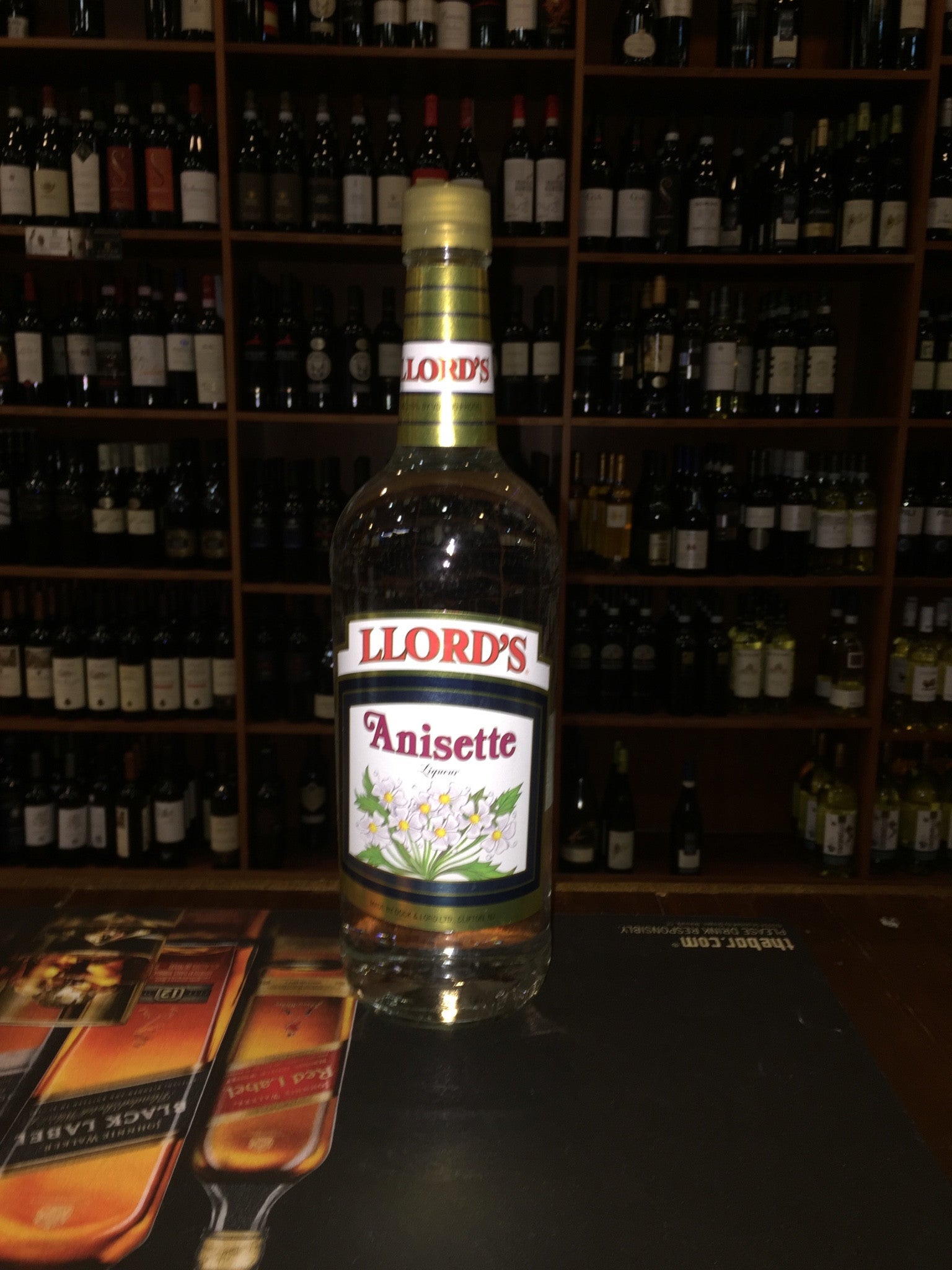 Llord's Anisette 1L a tall glass clear bottle with a white label a golden plastic top