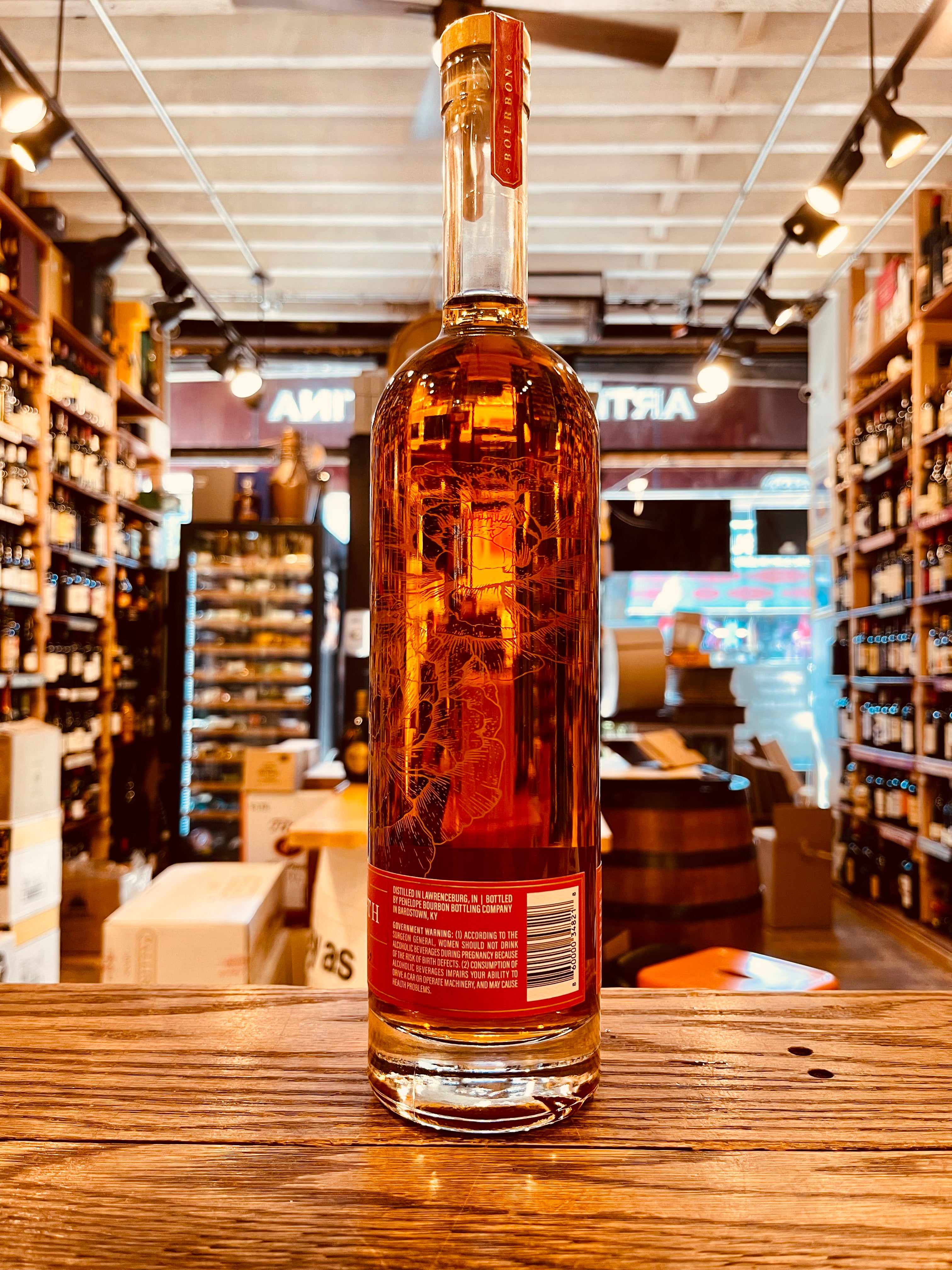 Penelope Bourbon Barrel Strength 750mL the backside of a tall clear glass bottle with a slender long neck with red label and an image of a rose etched onto the bottle