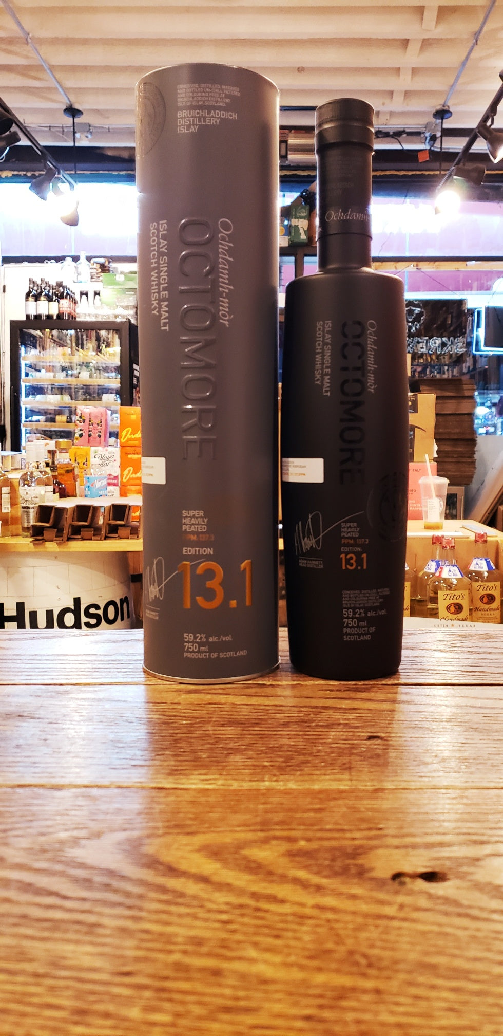 Octomore 13.1 118.4 750mL a tall gray cylinder next to a tall round shouldered slender black frosted glass bottle