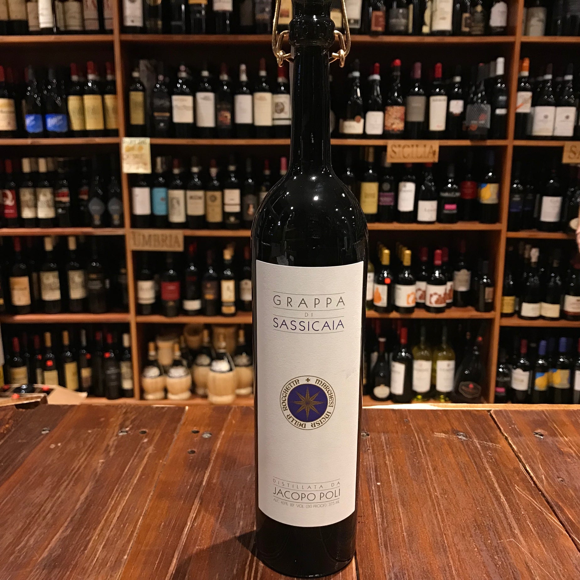 Sassicaia Grappa 375mL a tall slender dark bottle with a slender thin neck a large white label and a pop topper