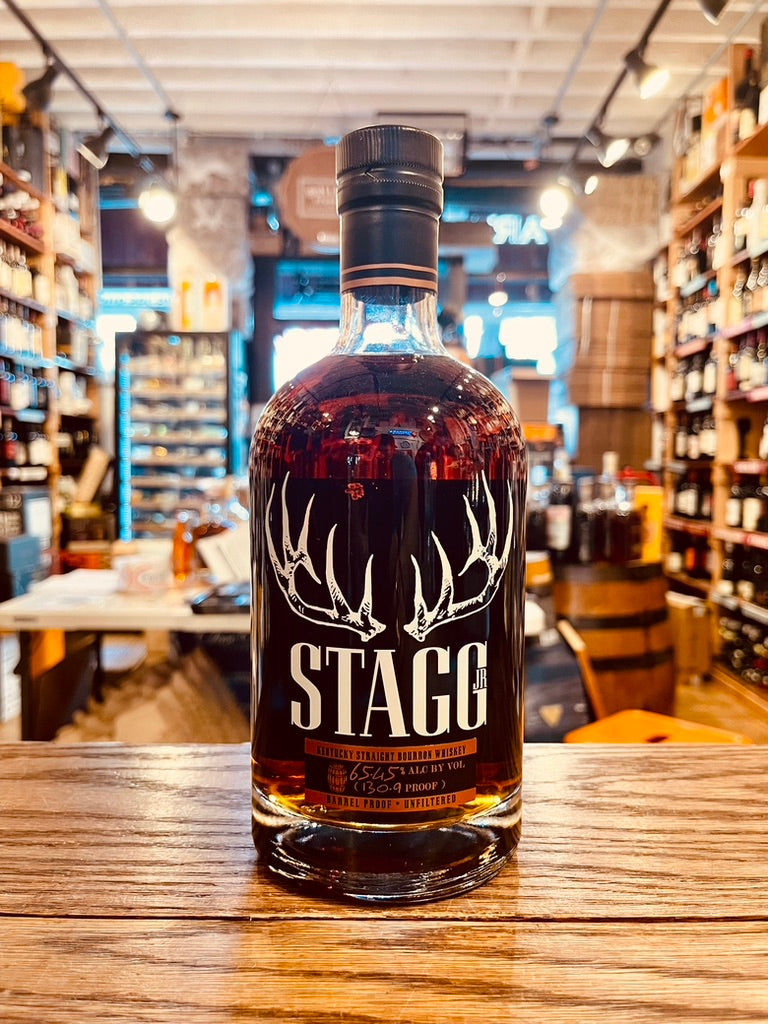 Stagg 127.9 750mL a short round shouldered clear glass bottle with white lettering and the image of deer antlers on it with a black top