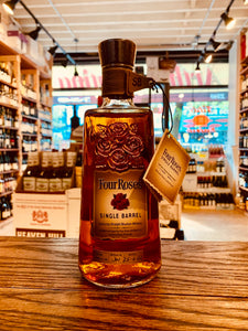 Four Roses Single Barrel 750mL a square rounded clear bottle with an engraving of four roses on the glass with a beige burnt label and leather necker with a wooden top