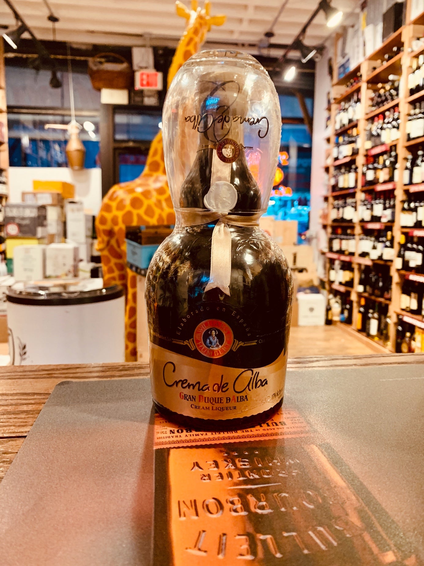 Crema De Alba 750mL Williams Humbert small rounded squat dark bottle with a gold label and a glass over the top of the bottle