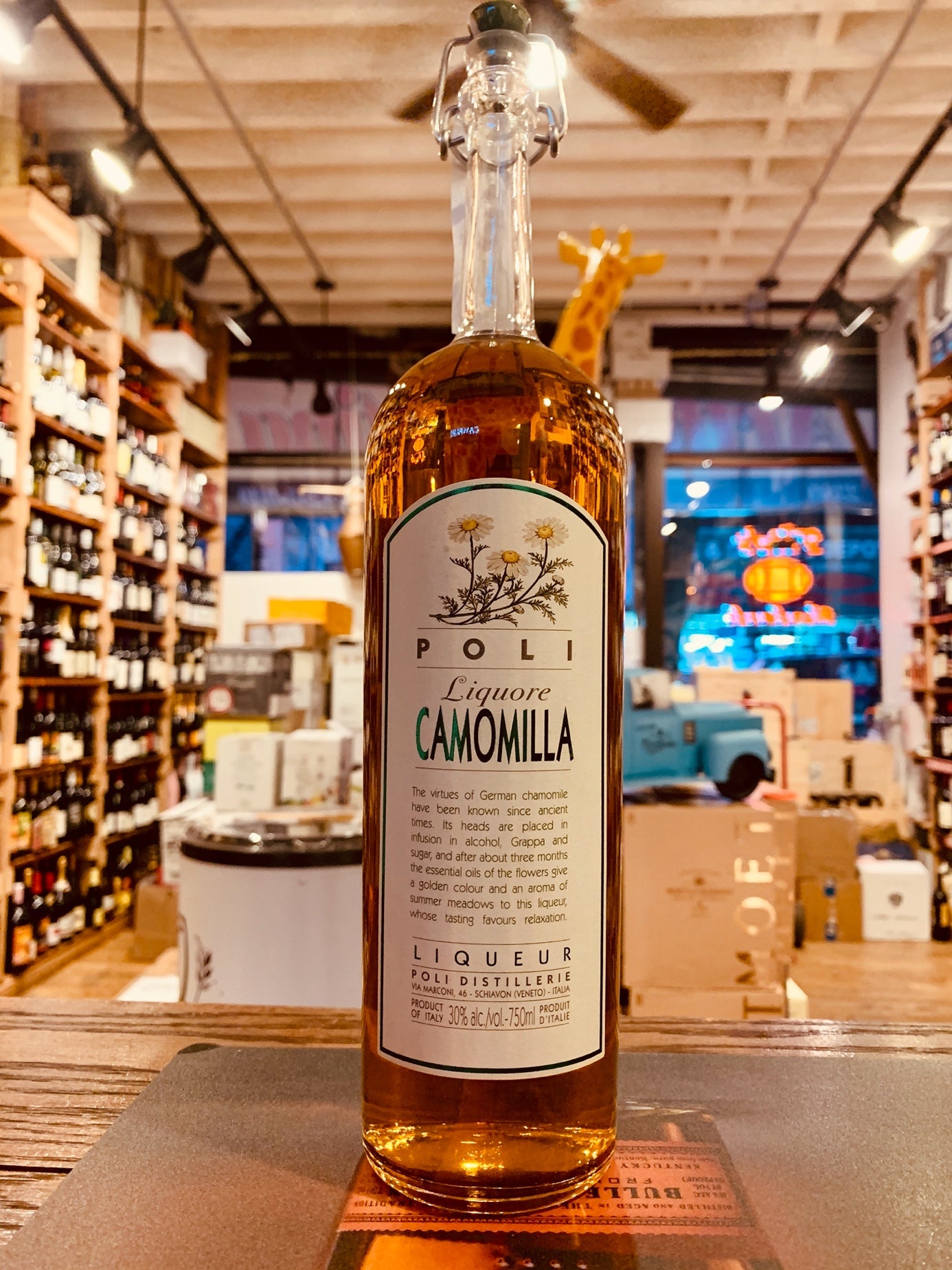 Poli Camomilla Liqueur 750mL a tall slender clear glass bottle with a thing slender neck and pop top with a large white label