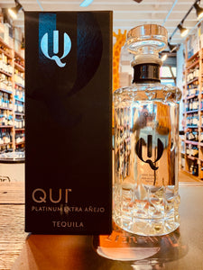 Qui Platinum Extra Anejo 750mL a black box with silver lettering next to a cylinder shaped clear glass bottle with black lettering and a glass topper