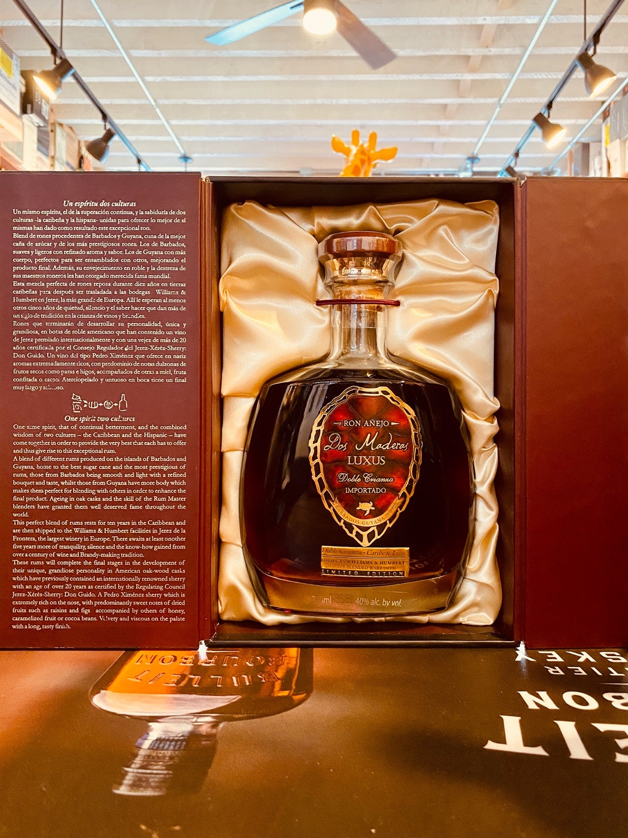Dos Maderas Rum Luxus 750mL an open maroon colored box with a squat short rounded bottle inside a silk backing with a ruby red label and wooden top