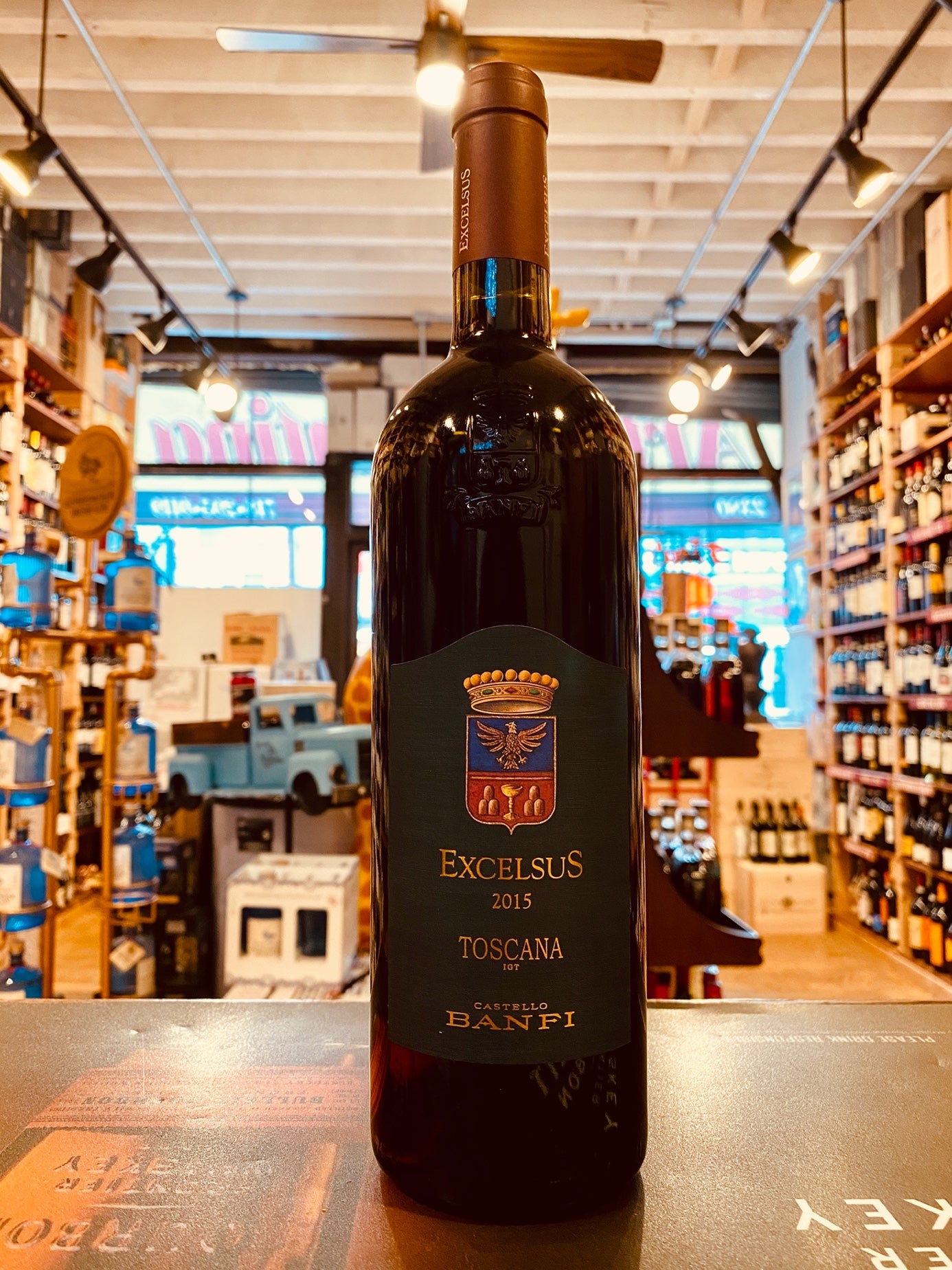 Excelsus Toscana 750mL tall dark wine bottle with a dark green label with a coat of arms emblem and gold lettering with a dark gold top