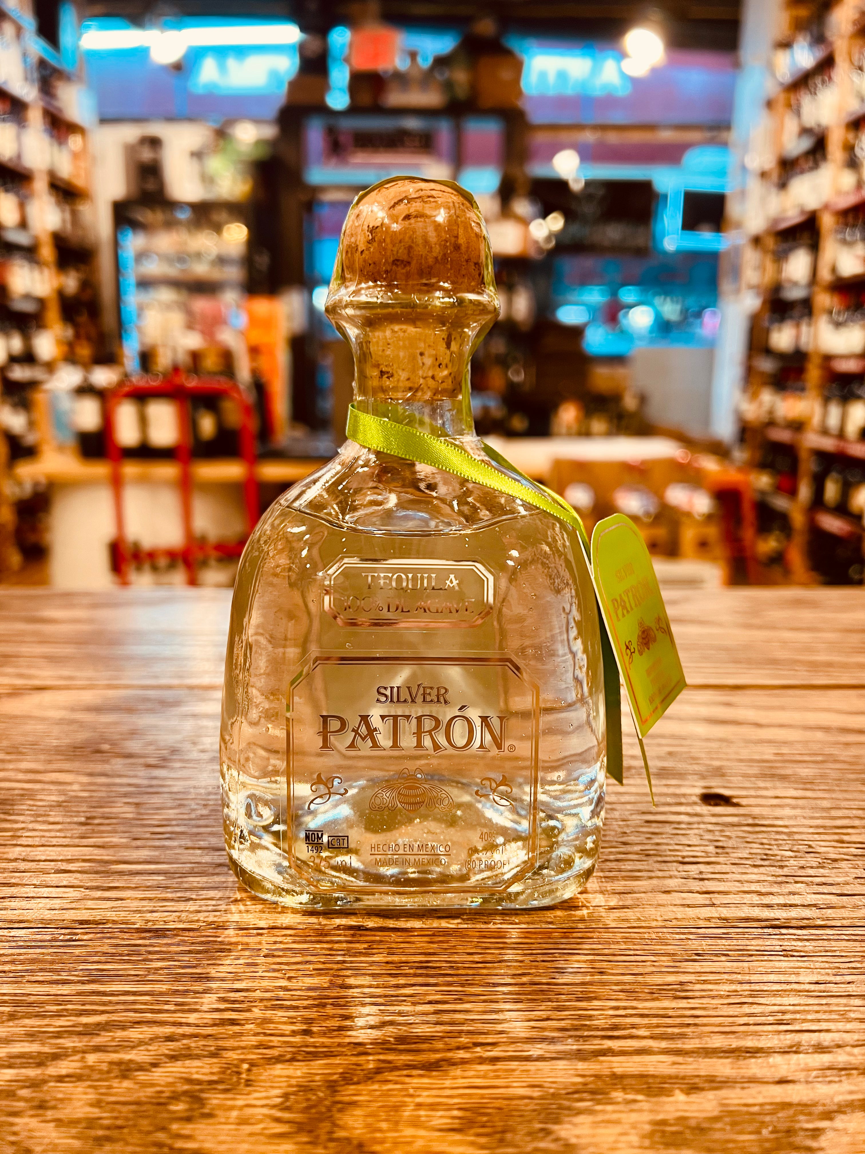 Patron Silver 375mL a small squat rounded clear glass bottle with silver lettering and a corked top with a green tag around the neck