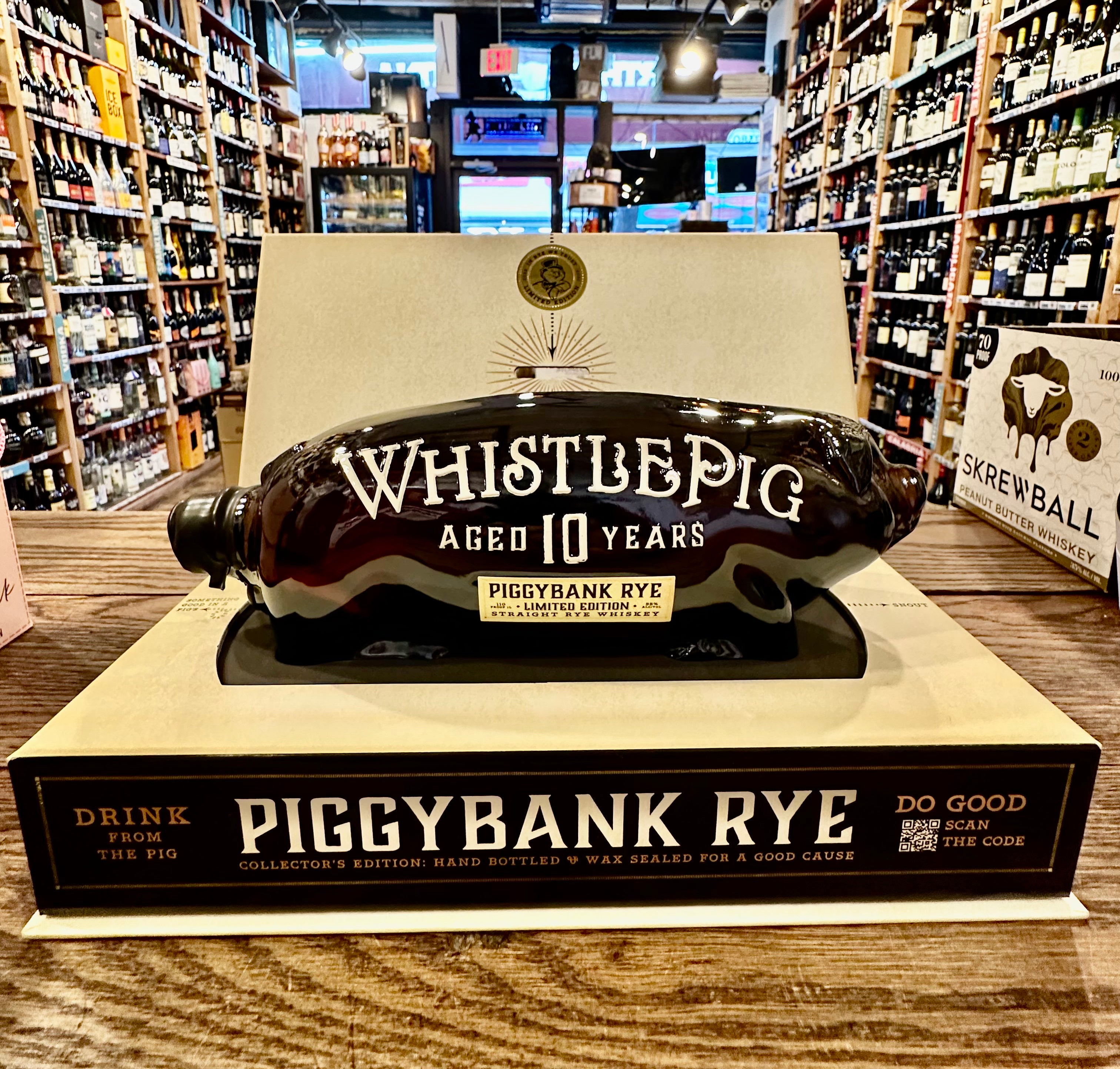 Whistle Pig Piggybank Rye 1L a pig shaped clear glass bottle bottle with white lettering  sitting on top of a rectangle shaped box stand that is beige and black in color