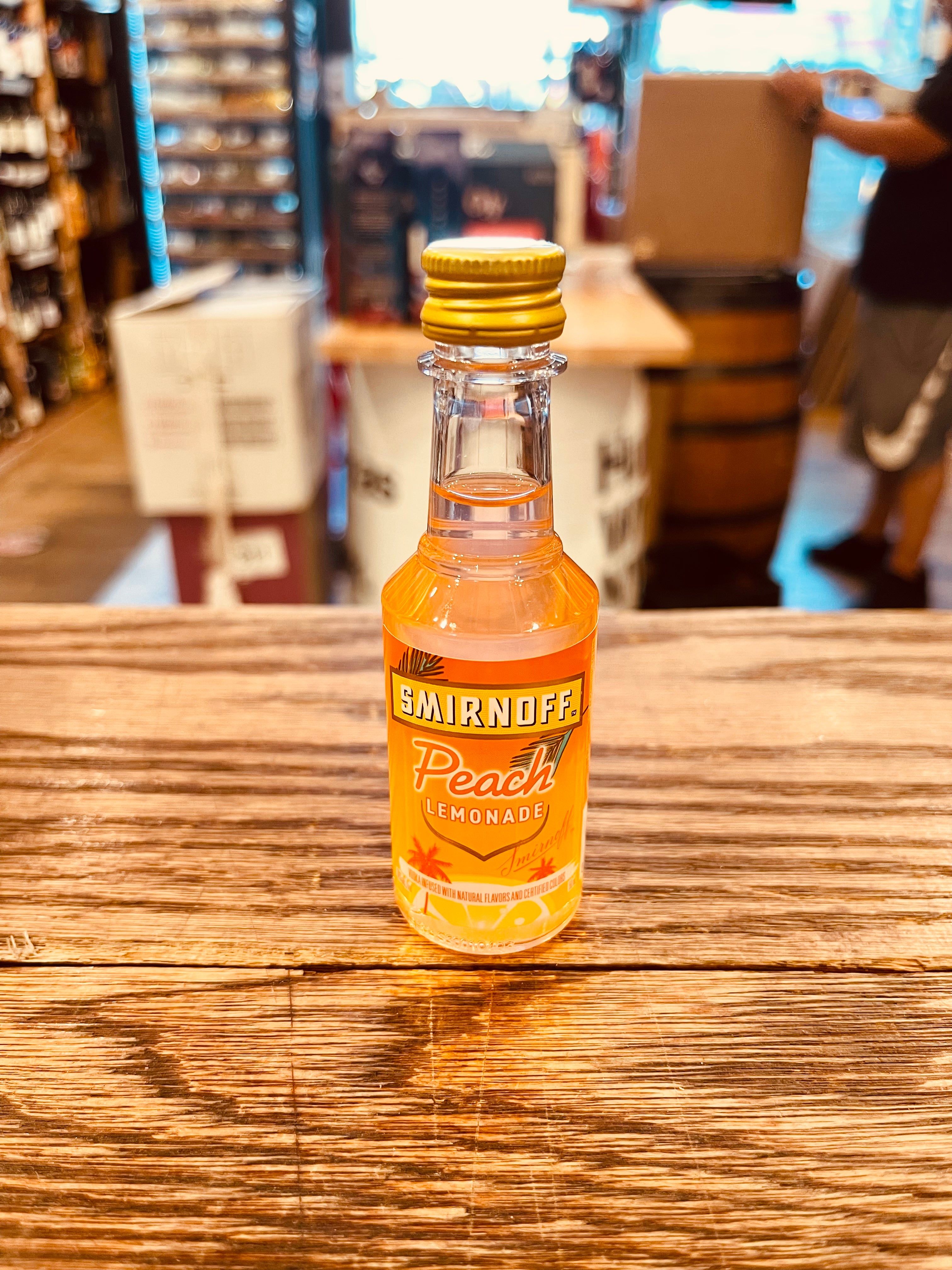 Smirnoff Peach Lemonade 50mL a small clear plastic bottle with an orange label and golden top