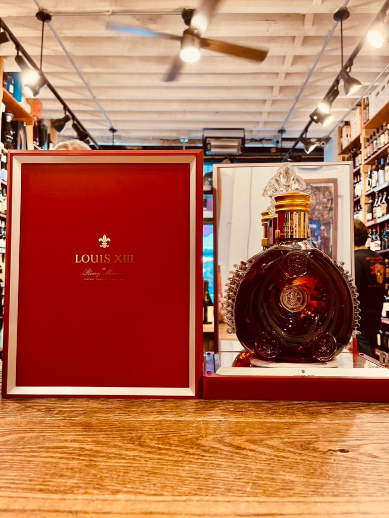 Louis XIII a red box next to a clear crystal glass rounded bottle with a golden top 